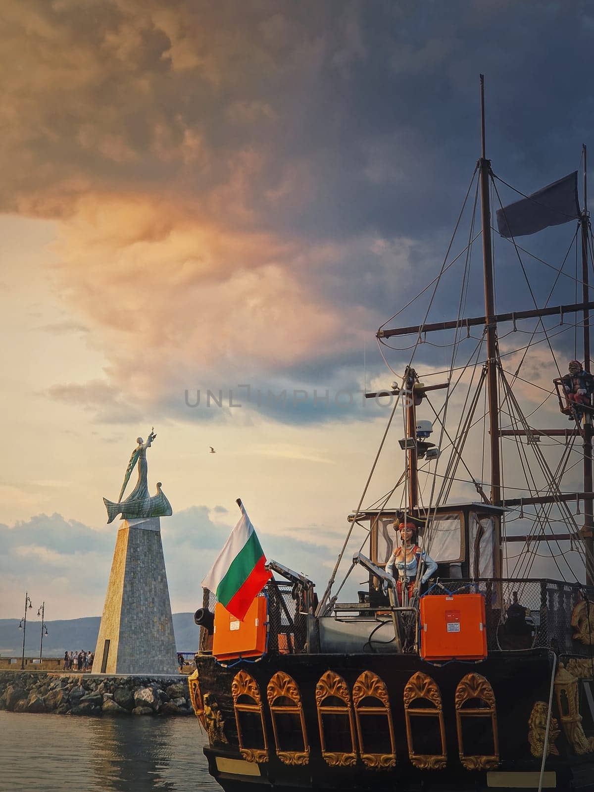 Statue of Saint Nicholas the patron of sailors, in the old town of Nessebar, Burgas, Bulgaria. Sunset scene at the coastline with a sail ship moored at the deck