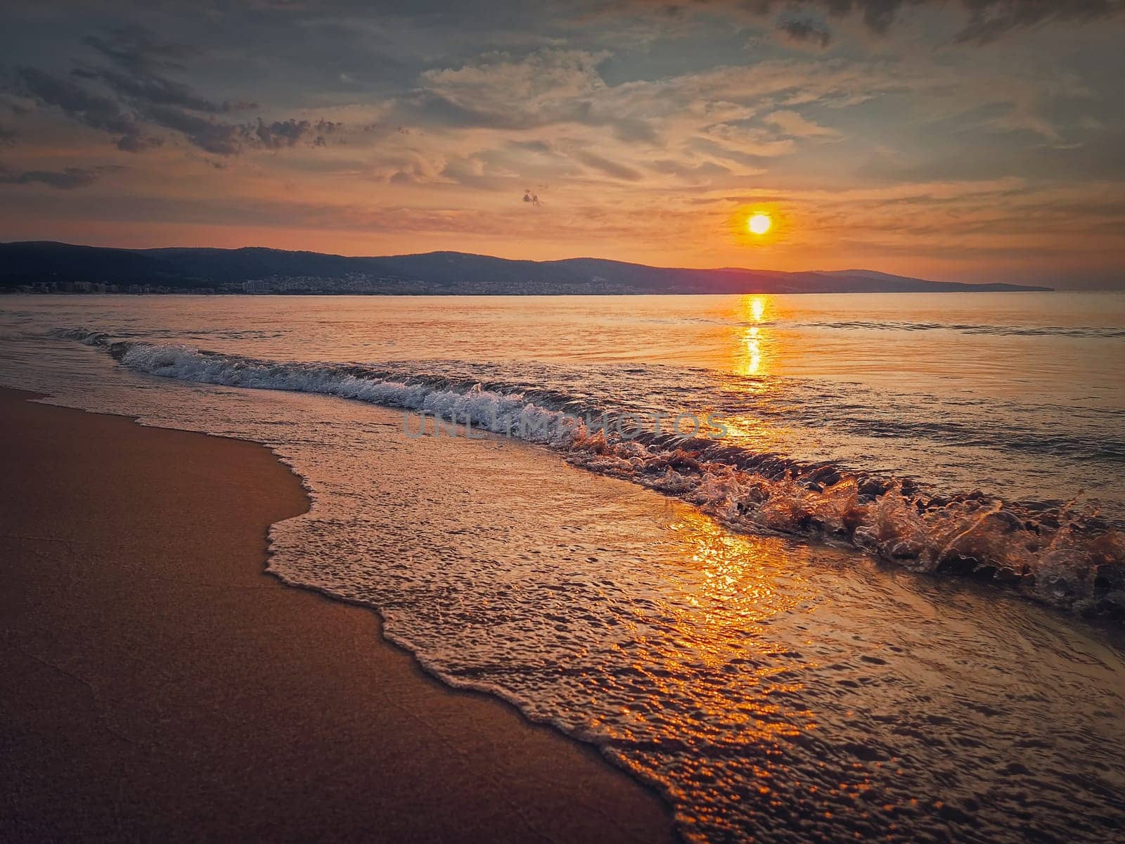 Peaceful seascape, silent morning seaside with beautiful sunrise above the hills and foamy waves hitting the sand. Dawn at the sea, travel background