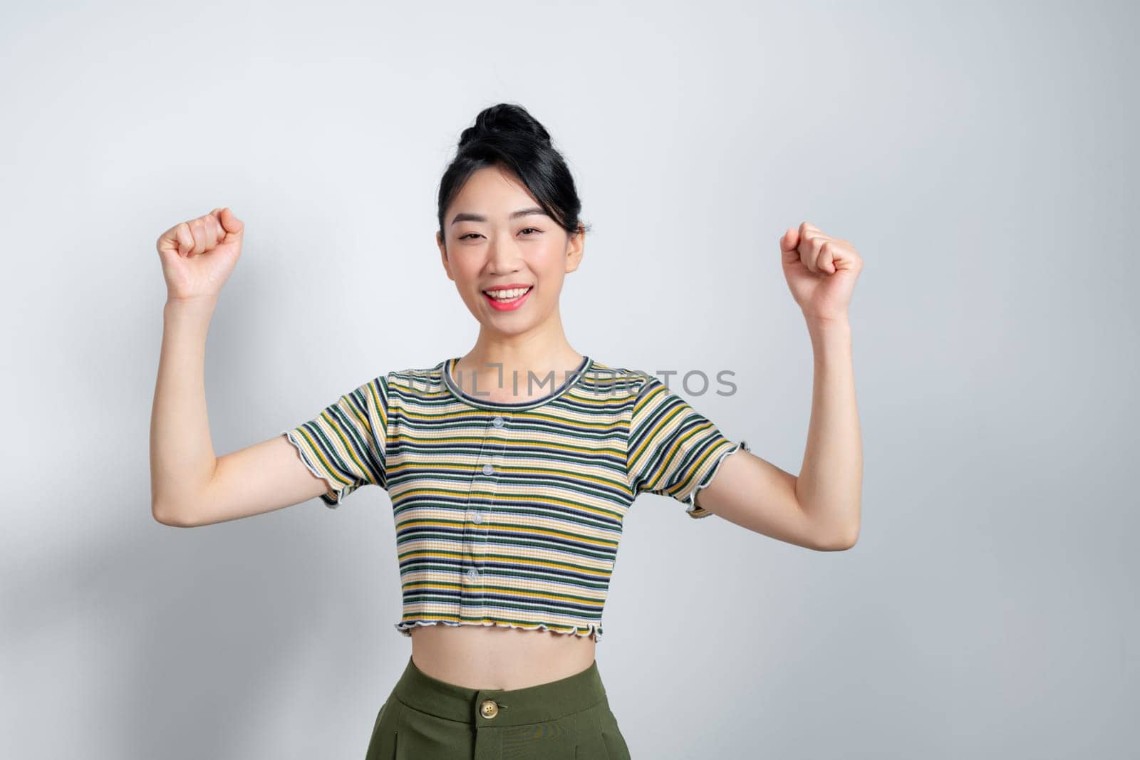 Beautiful Asian woman raises arms and fists clenched with celebrating victory expressing success.