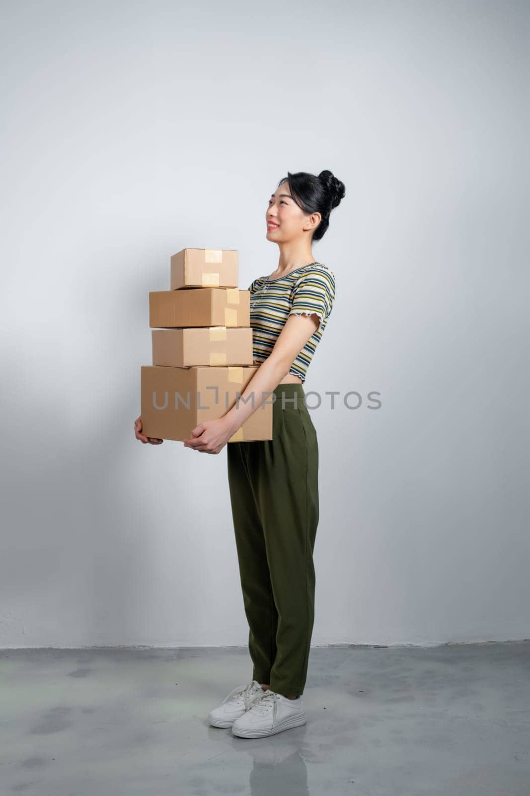 Beautiful young woman is holding cardboard box on gray background. by makidotvn