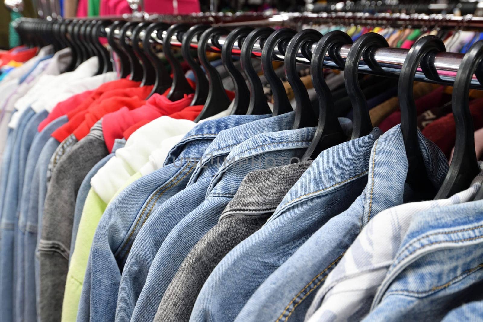 Denim jackets and shirts hanging in row in a store by olgavolodina