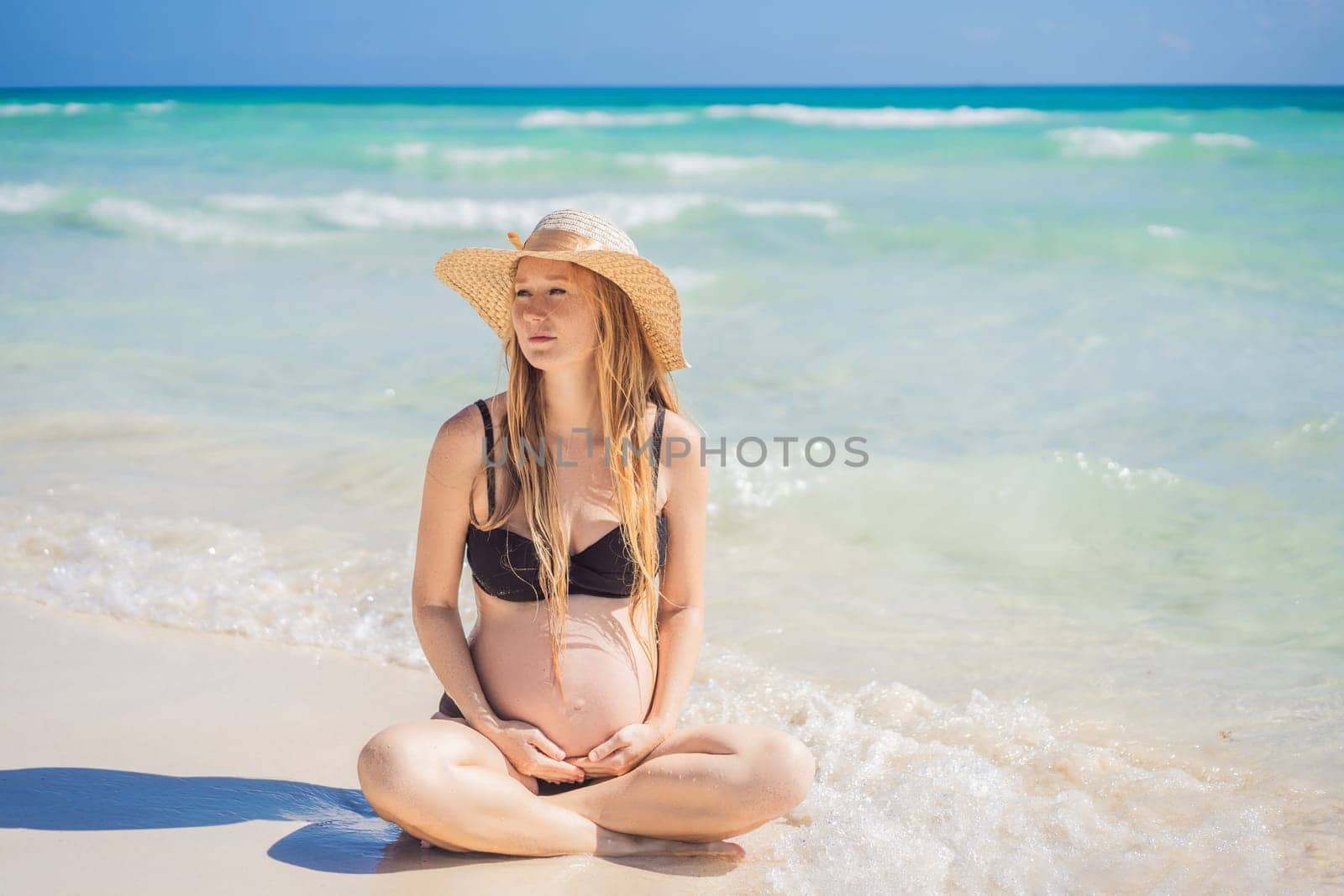 Radiant and expecting, a pregnant woman stands on a pristine snow-white tropical beach, celebrating the miracle of life against a backdrop of natural beauty.