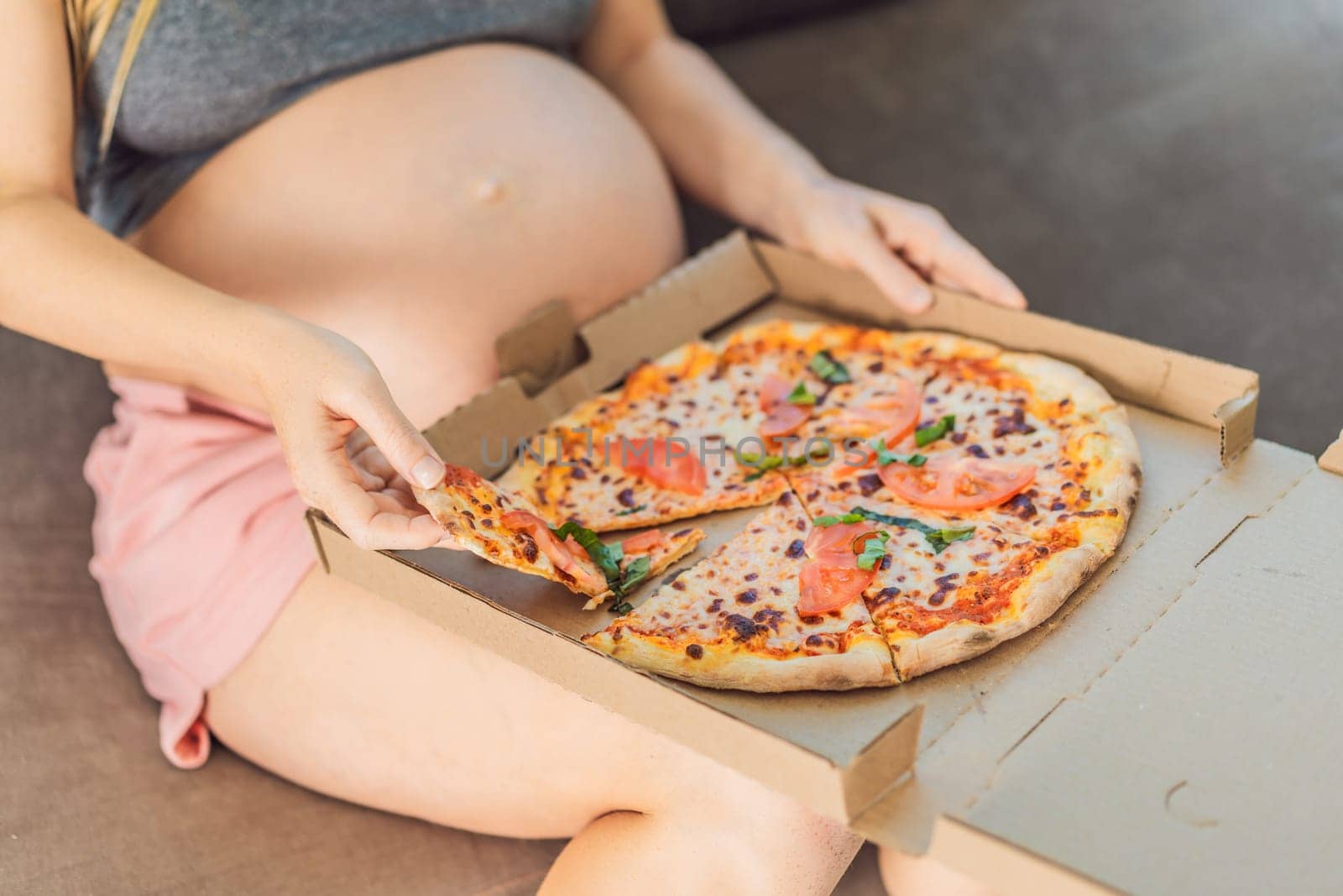 A pregnant woman enjoys a slice of pizza, savoring a moment of indulgence while satisfying her craving for a delightful, comforting treat. Excited Pregnant Young Lady Enjoying Pizza Holding Biting Tasty Slice Posing With Carton Box. Junk Food Lover Eating Italian Pizza. Unhealthy Nutrition Cheat Meal by galitskaya