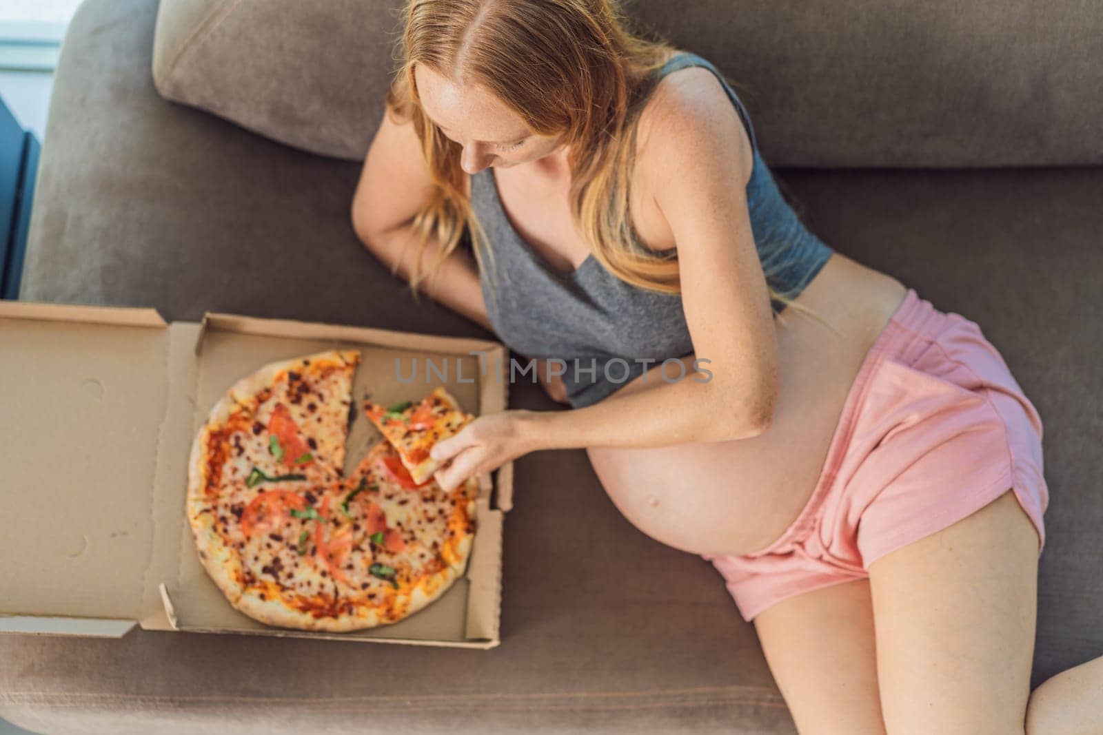 A pregnant woman enjoys a slice of pizza, savoring a moment of indulgence while satisfying her craving for a delightful, comforting treat. Excited Pregnant Young Lady Enjoying Pizza Holding Biting Tasty Slice Posing With Carton Box. Junk Food Lover Eating Italian Pizza. Unhealthy Nutrition Cheat Meal by galitskaya