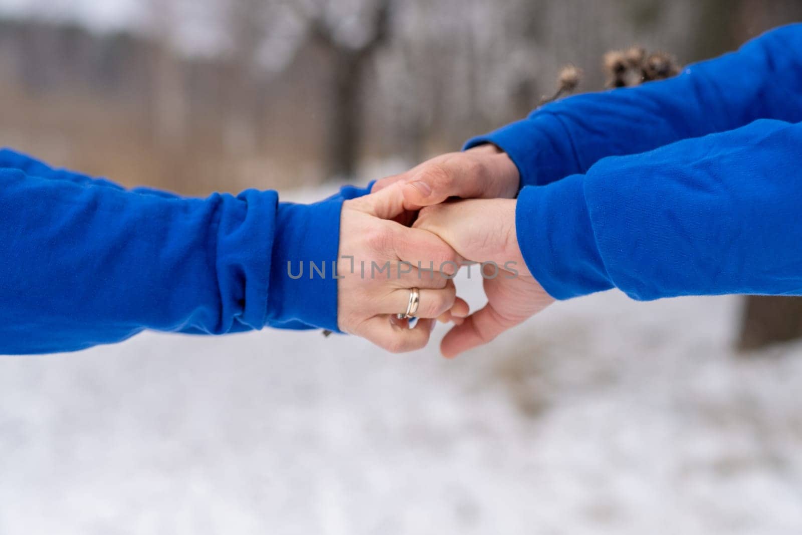 Outdoor happy couple in love posing in cold winter weather. A man and a woman in blue hoodies. Emotional young couple having fun while walking by winter forest, loving man hugging his laughing woman