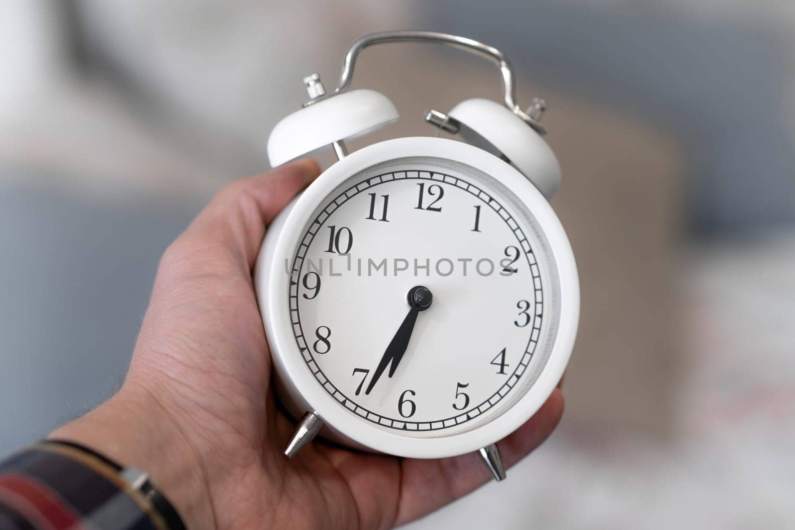 Round white alarm clock in a man's hand close-up. The hands on the clock show half past seven in the morning, time to get up. Retro alarm clock on the table, vintage tone. space for text