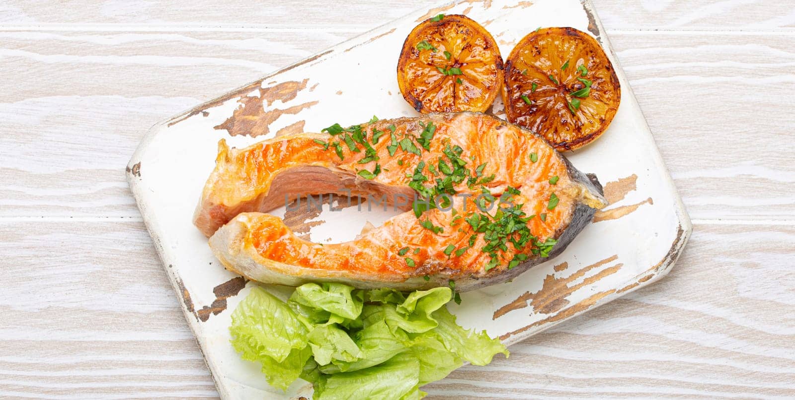 Grilled fish salmon steak and green salad with lemon served on white cutting board rustic wooden background top view, balanced diet or healthy nutrition meal with salmon and veggies.