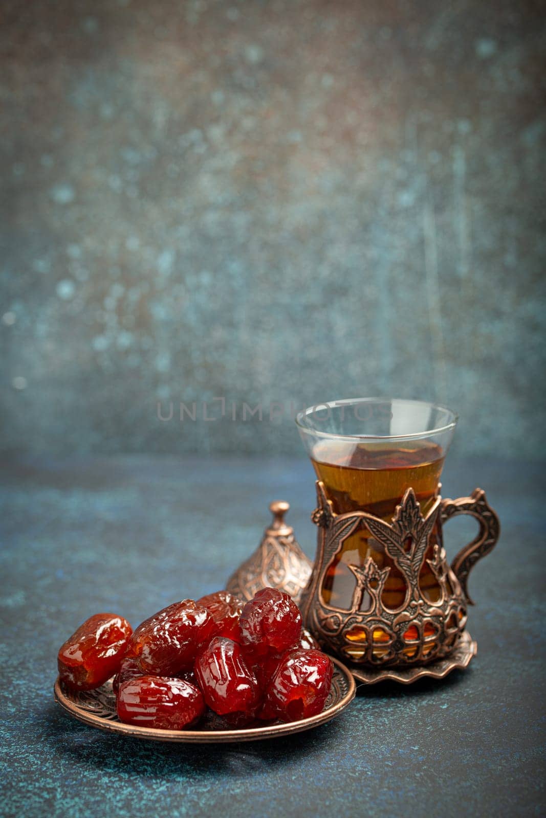 Breaking fasting with dried dates during Ramadan Kareem, Iftar meal with dates and Arab tea in traditional glass, angle view on rustic blue background. Muslim feast by its_al_dente
