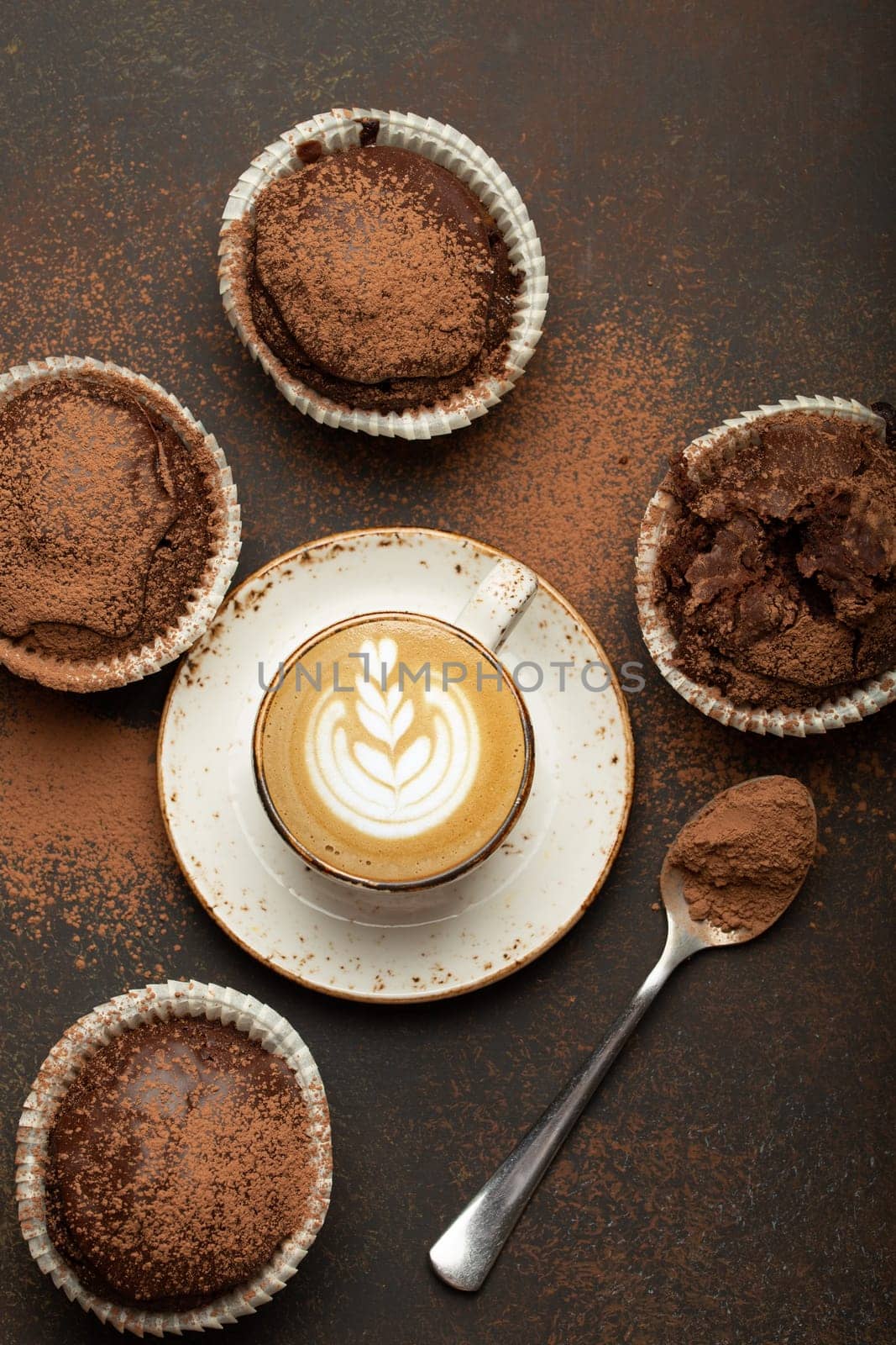 Chocolate and cocoa browny muffins with coffee cappuccino in cup top view on brown rustic stone background, sweet homemade dark chocolate cupcakes.