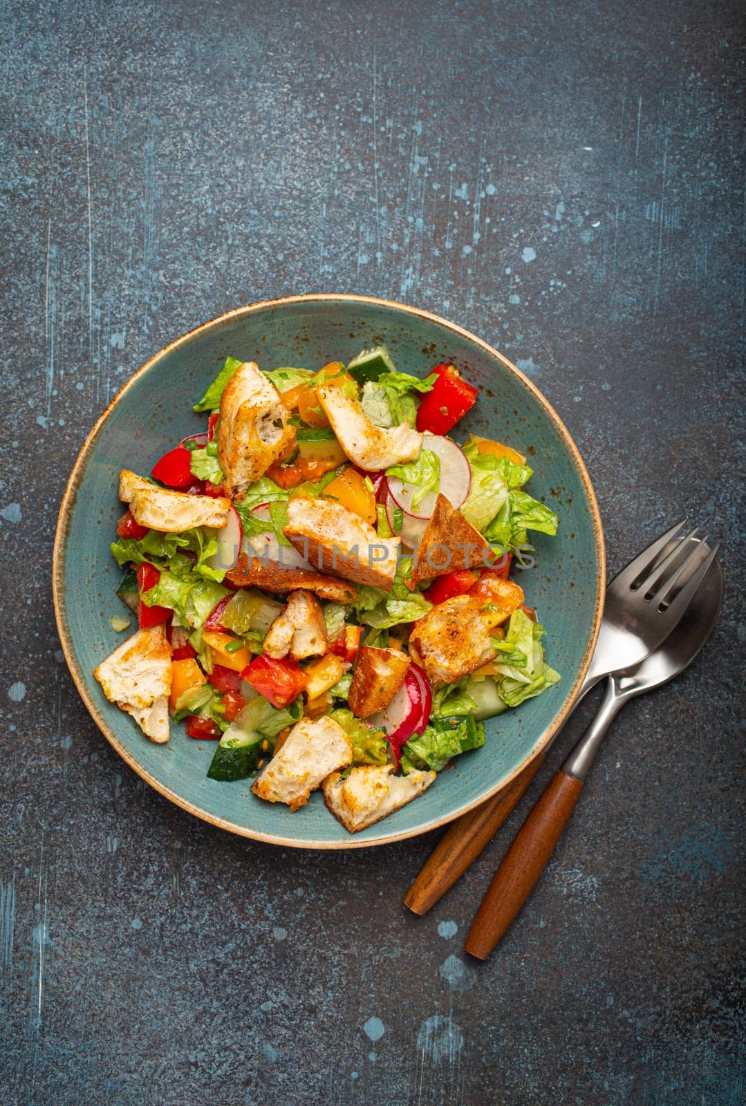 Traditional Levant dish Fattoush salad, Arab cuisine, made with pita bread croutons, vegetables and herbs. Healthy Middle Eastern vegetarian salad on plate, rustic dark blue background top view.