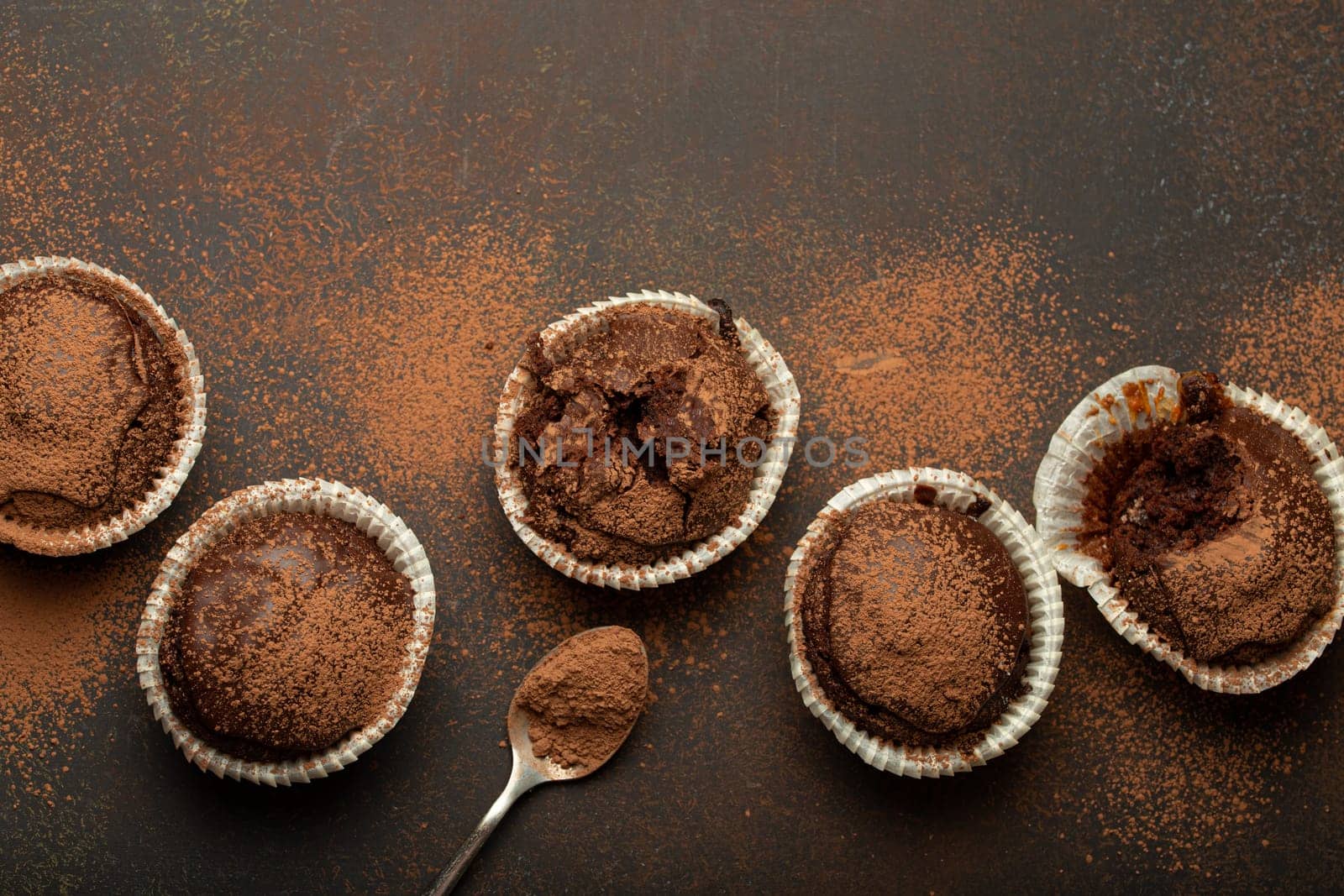 Chocolate browny muffins and cocoa in teaspoon top view on brown rustic stone background, sweet homemade dark chocolate cupcakes.