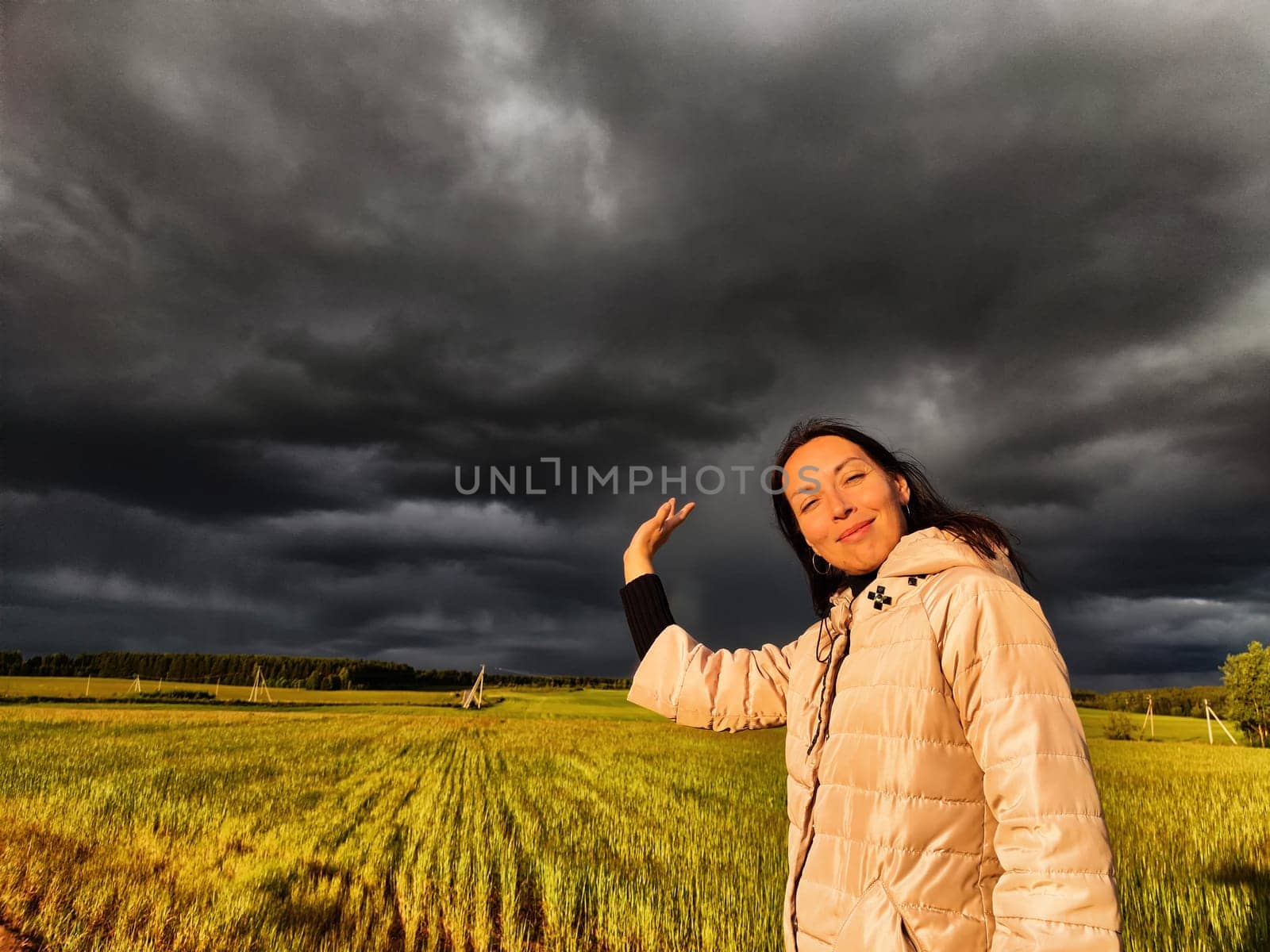 An adult girl in a field and with stormy sky with clouds posing for picture in the rain. A woman having fun outdoors on rural and rustic nature