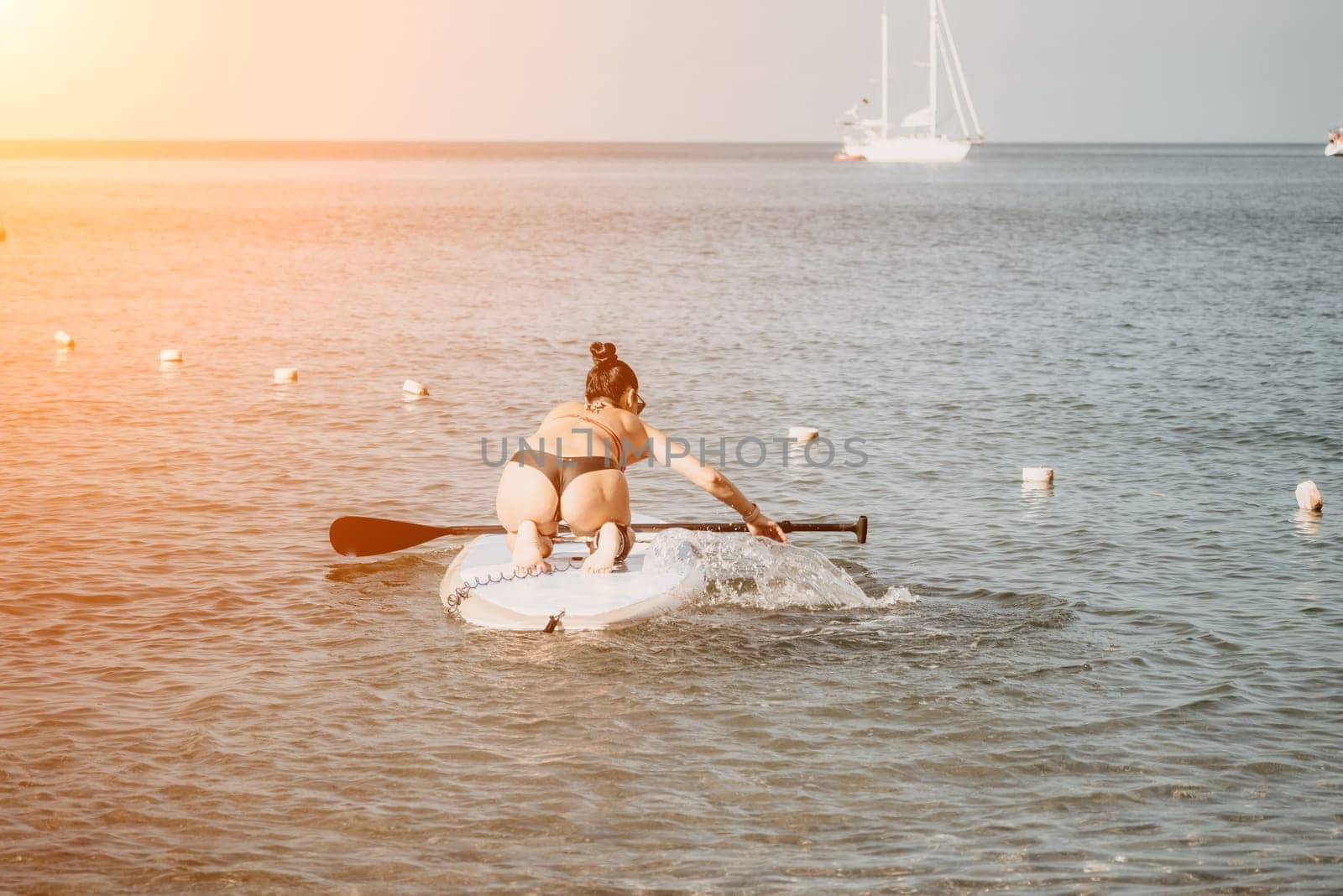 Sea woman sup. Silhouette of happy middle aged woman in rainbow bikini, surfing on SUP board, confident paddling through water surface. Idyllic sunset. Active lifestyle at sea or river