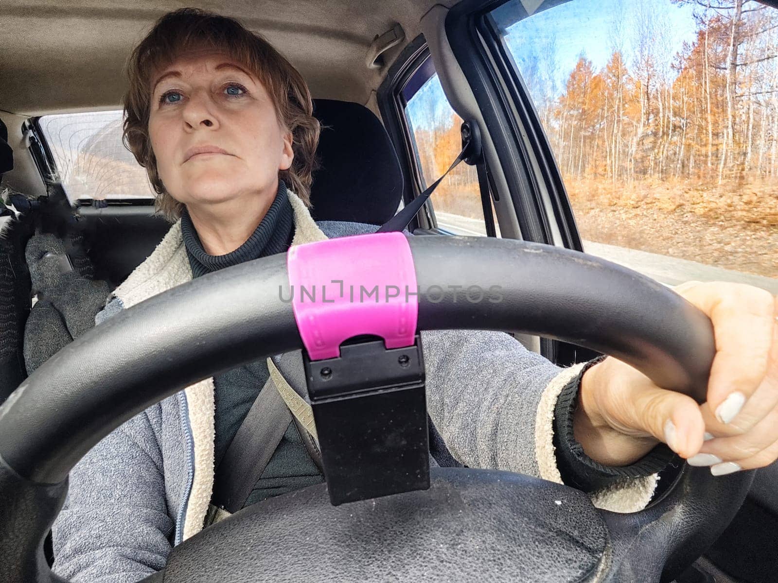 Portrait of female driver in solo journey. Adult mature woman holding steering wheel and looking through windscreen in travel by vehicle on vacation. Lady girl who is owner or rent a car for travel by keleny