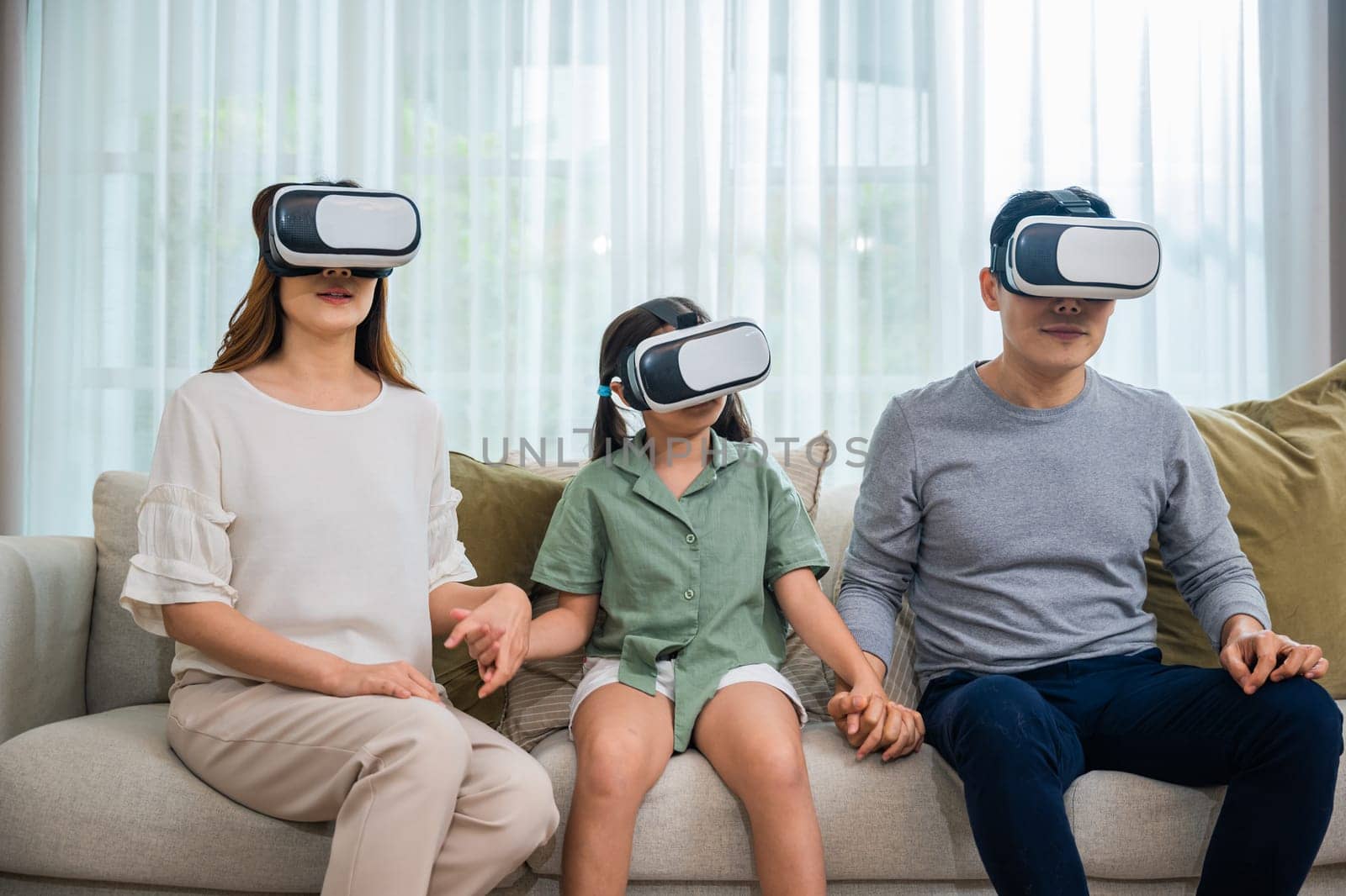 Asian family wear vr glasses headsets sitting on sofa in living room by Sorapop