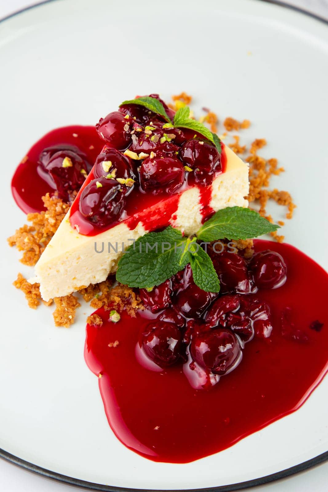 side view of cheesecake with juicy berries and mint on a white plate by tewolf