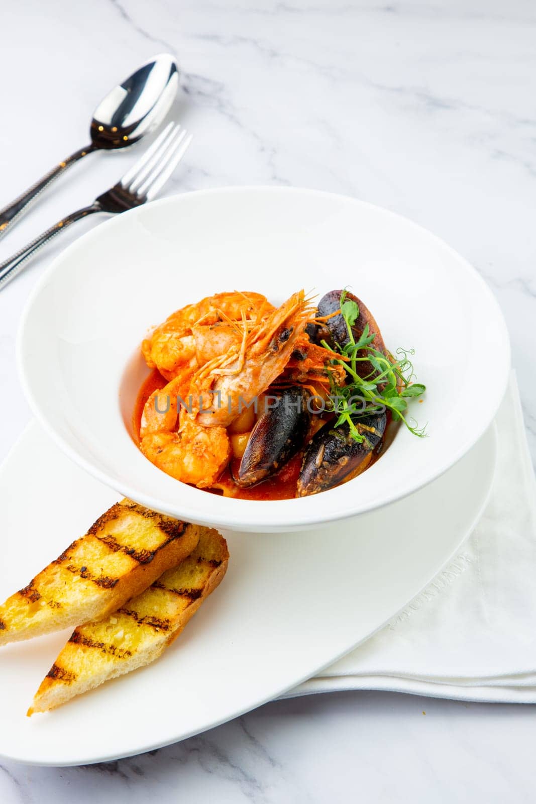 shrimp and mussels with herbs in a white plate with toasted bread, side view by tewolf