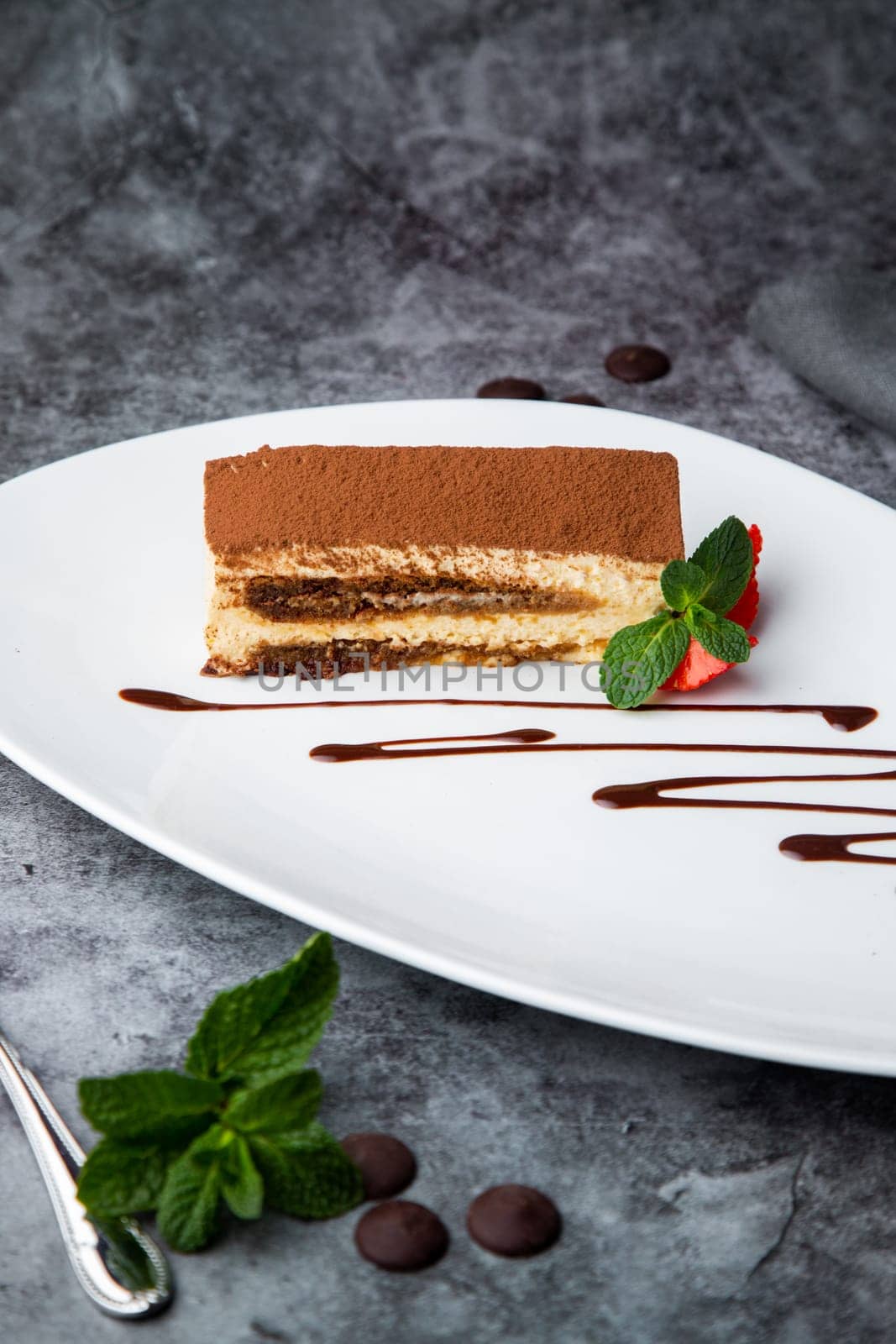 side view of chocolate sponge cake with strawberries and mint on a white plate by tewolf