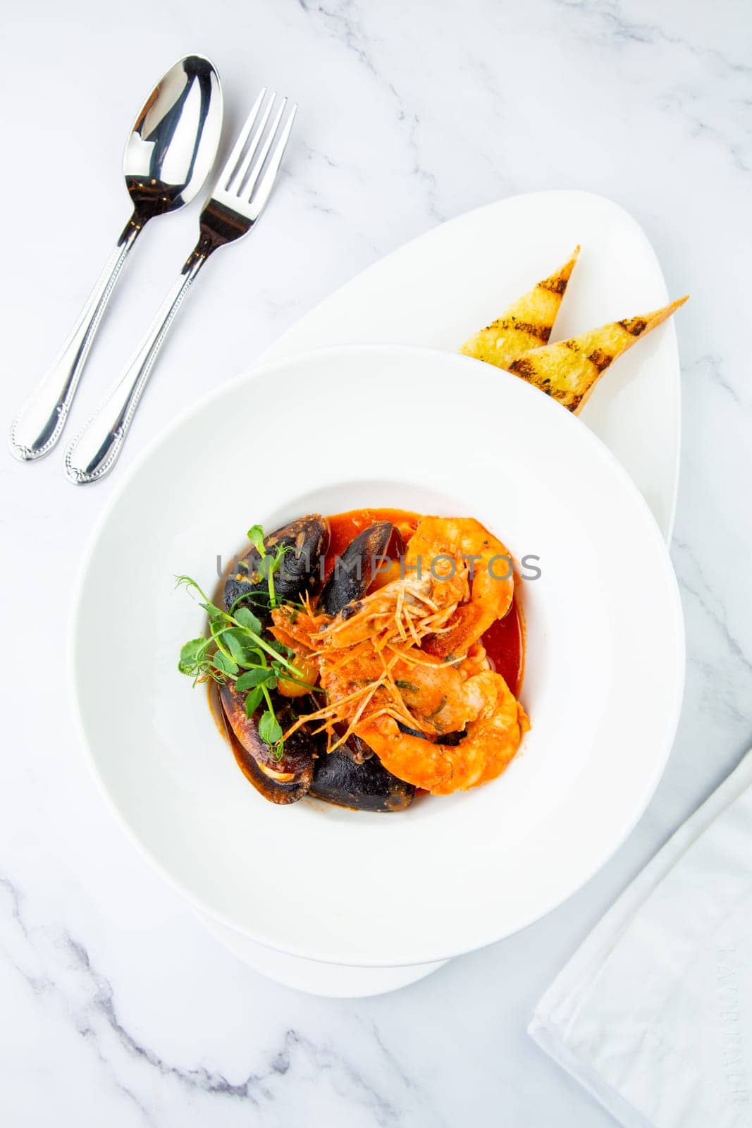 shrimp and mussels with herbs in a white plate with toasted bread, side view by tewolf