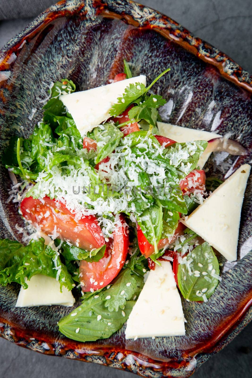 salad with herbs, tomatoes, grated cheese, sesame seeds and pieces of cheese, top view by tewolf