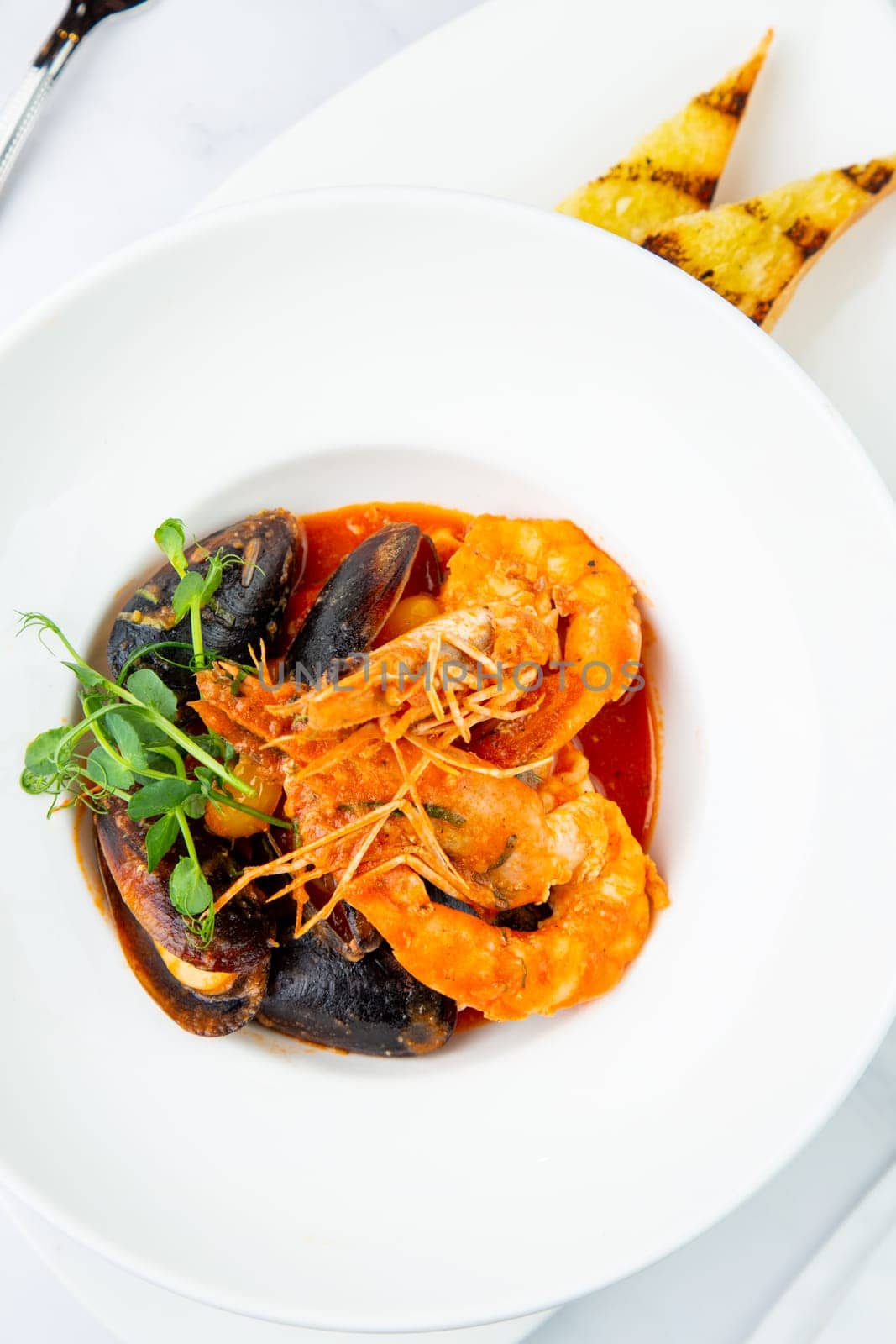 shrimp and mussels with herbs in a white plate with toasted bread, side view by tewolf