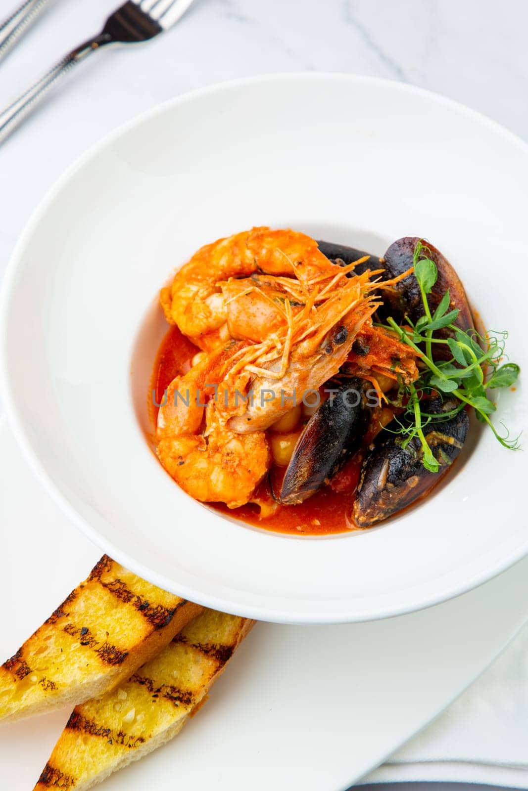 shrimp and mussels with herbs in a white plate with toasted bread, side view by tewolf