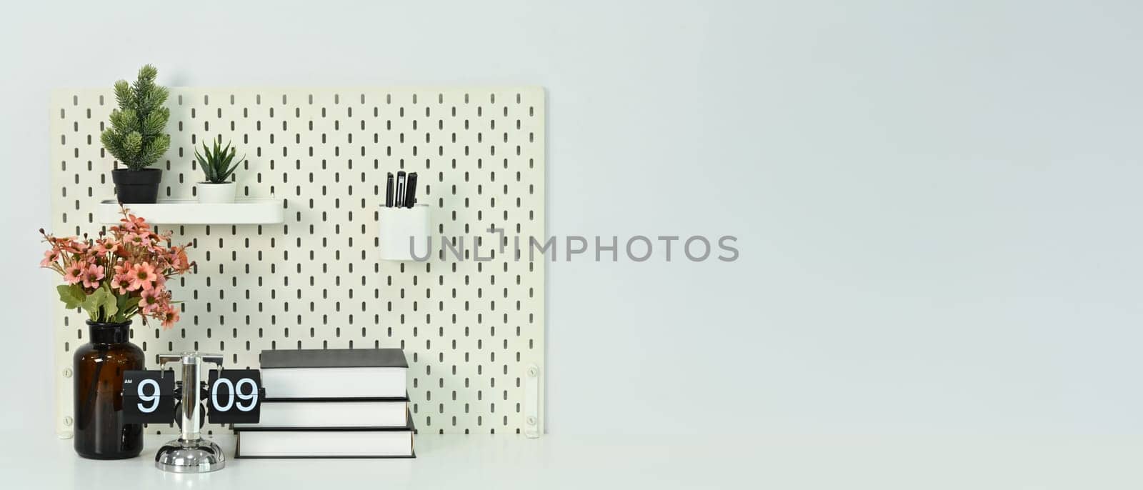 Books, vintage flip clock, and potted plants on white table against a clean white wall.