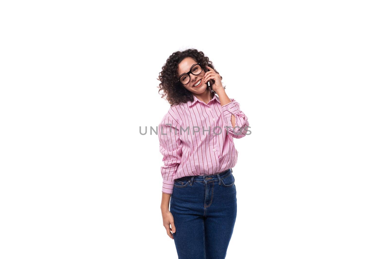 young European curly brunette lady in a pink blouse speaks on the phone against the background with copy space.