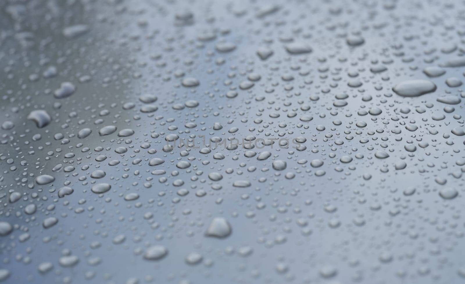 Raindrops on black hood of car. Rain on glass concept