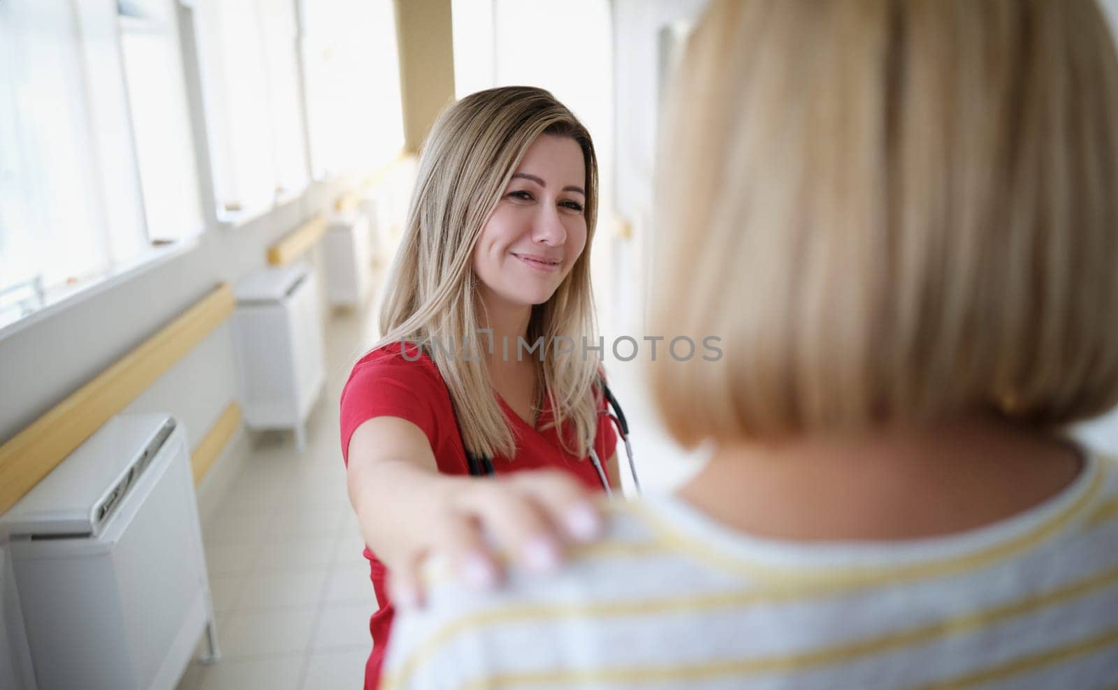 Smiling female doctor keeps hand on patient shoulder. Medical services and medical support concept