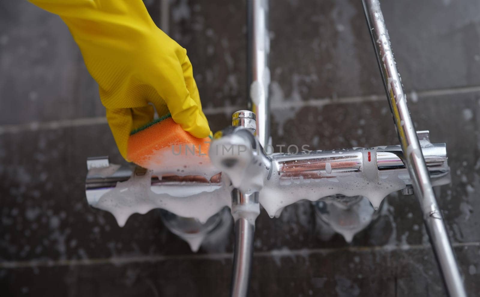 Cleaning lady in rubber glove washes faucet in bathroom with sponge with foam closeup. Cleaning company services concept