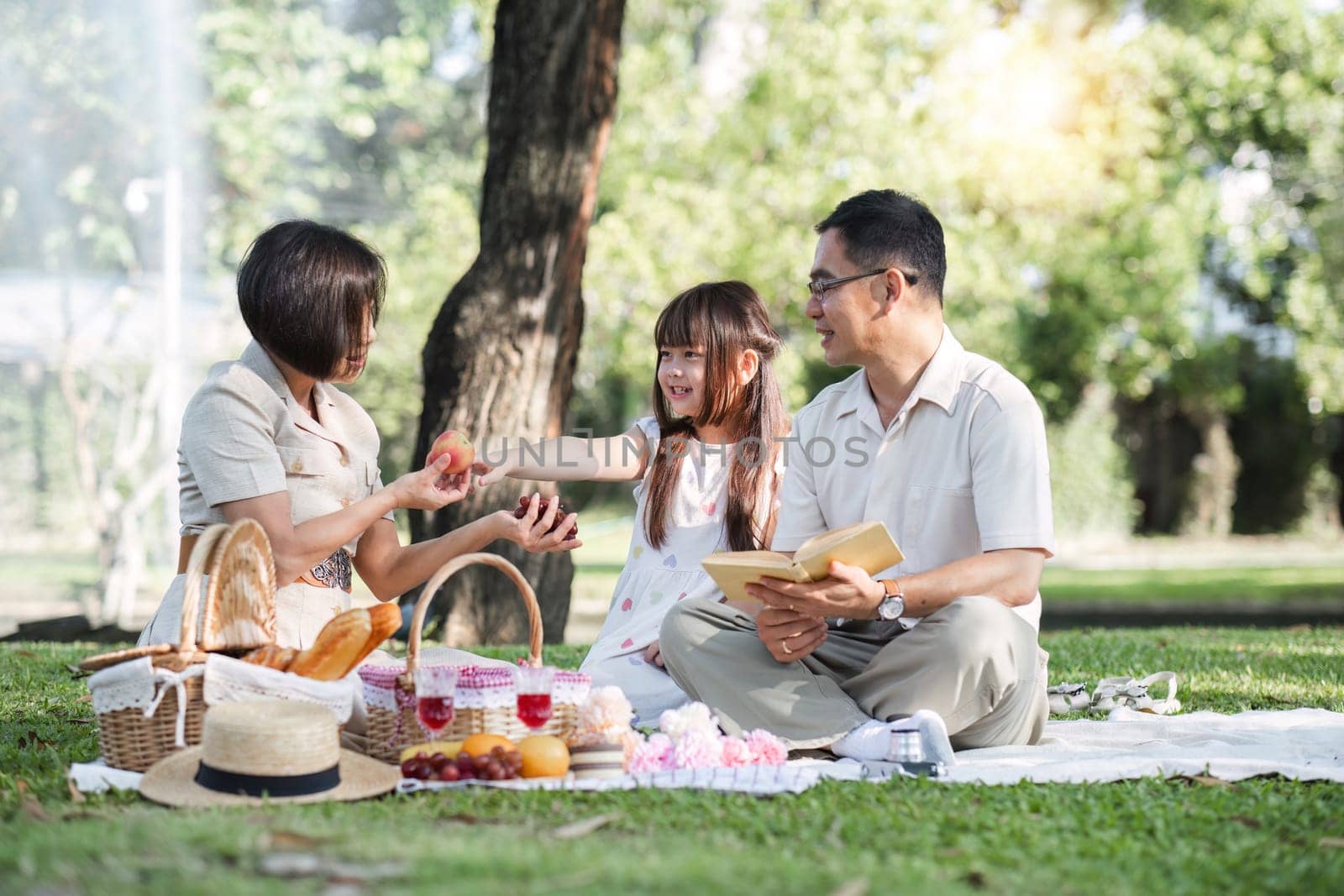 Family of senior couple and daughter picnicking in the park showing love Or reconnect after retirement in a relaxing park. An elderly man and a woman have fun on a mat in the backyard..