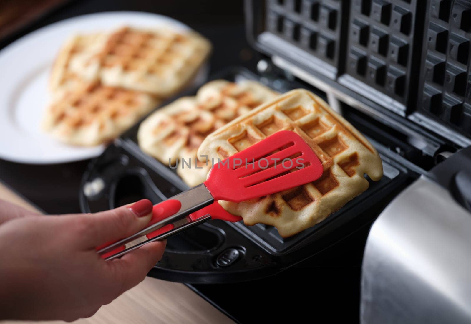 Female hands finishing making waffles on waffle iron in bakery. Persons preparing delicious meals in kitchen