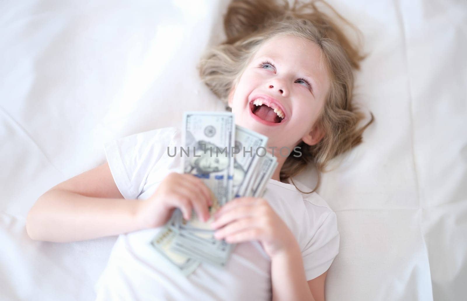 Little girl without front teeth holding money in her hands and smiling. Investment in pediatric dentistry concept