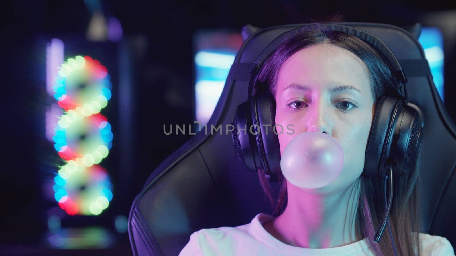 Young gamer woman sitting in a chair in gaming club and blowing a bubble gum, portrait