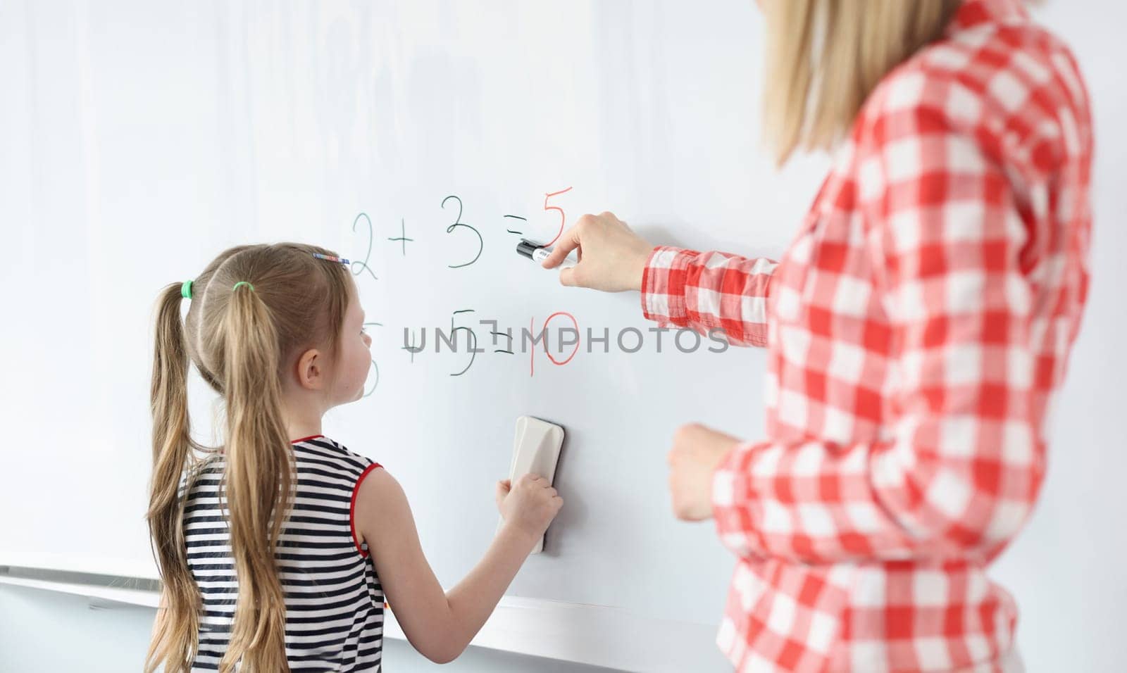 Little girl and teacher solving math equations on blackboard by kuprevich