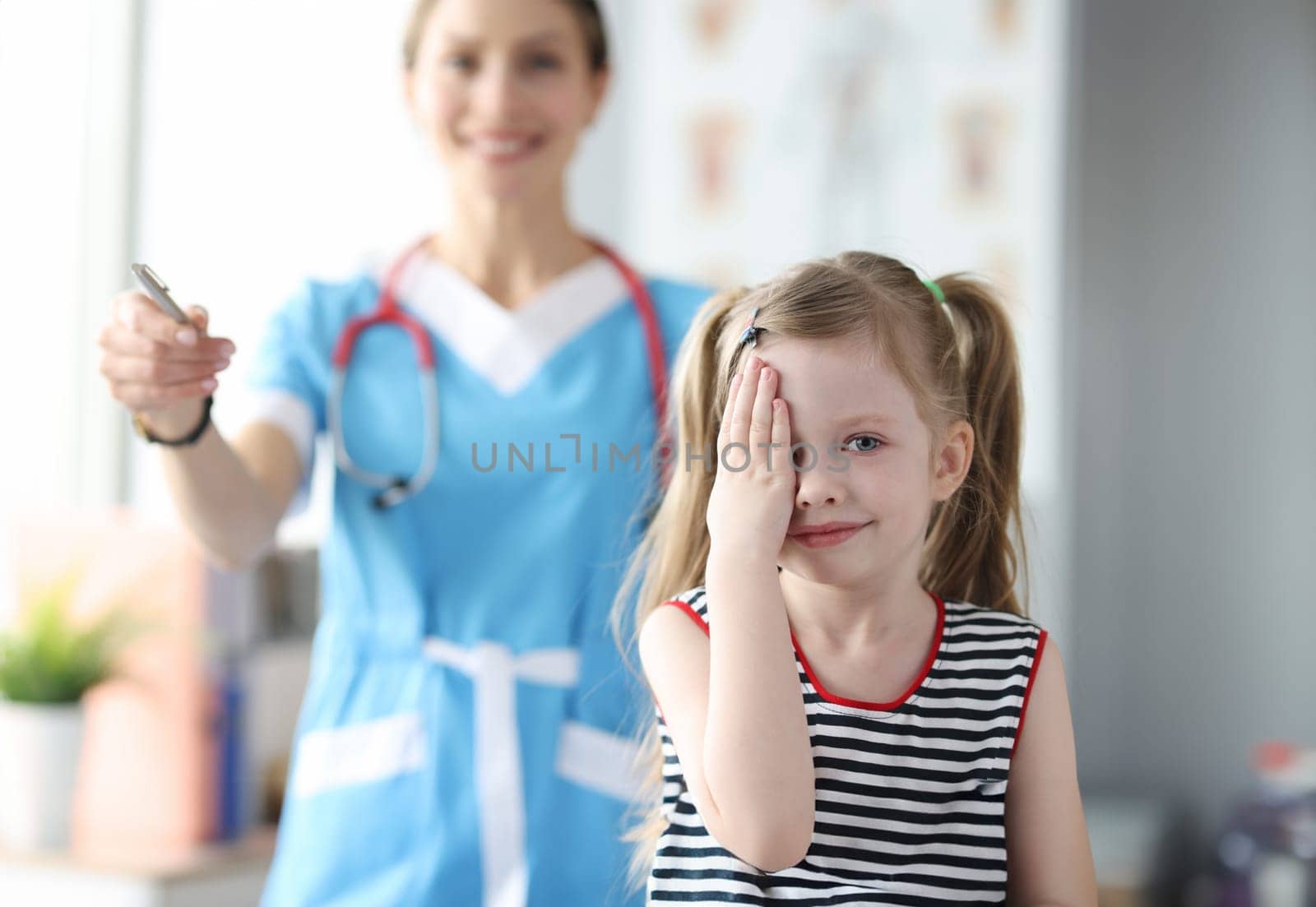 Little girl covering her eyes with her hand at ophthalmologist appointment. Eye examination in children concept