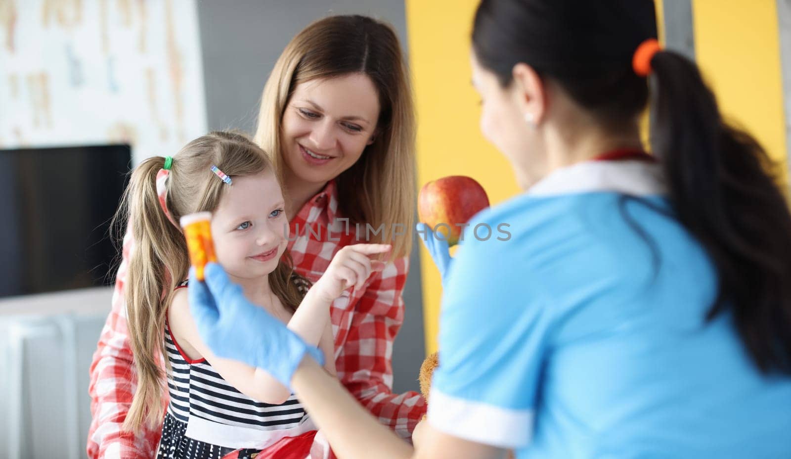 Doctor holding jar of medicine and apple in front of little girl and mother. Taking vitamins concept