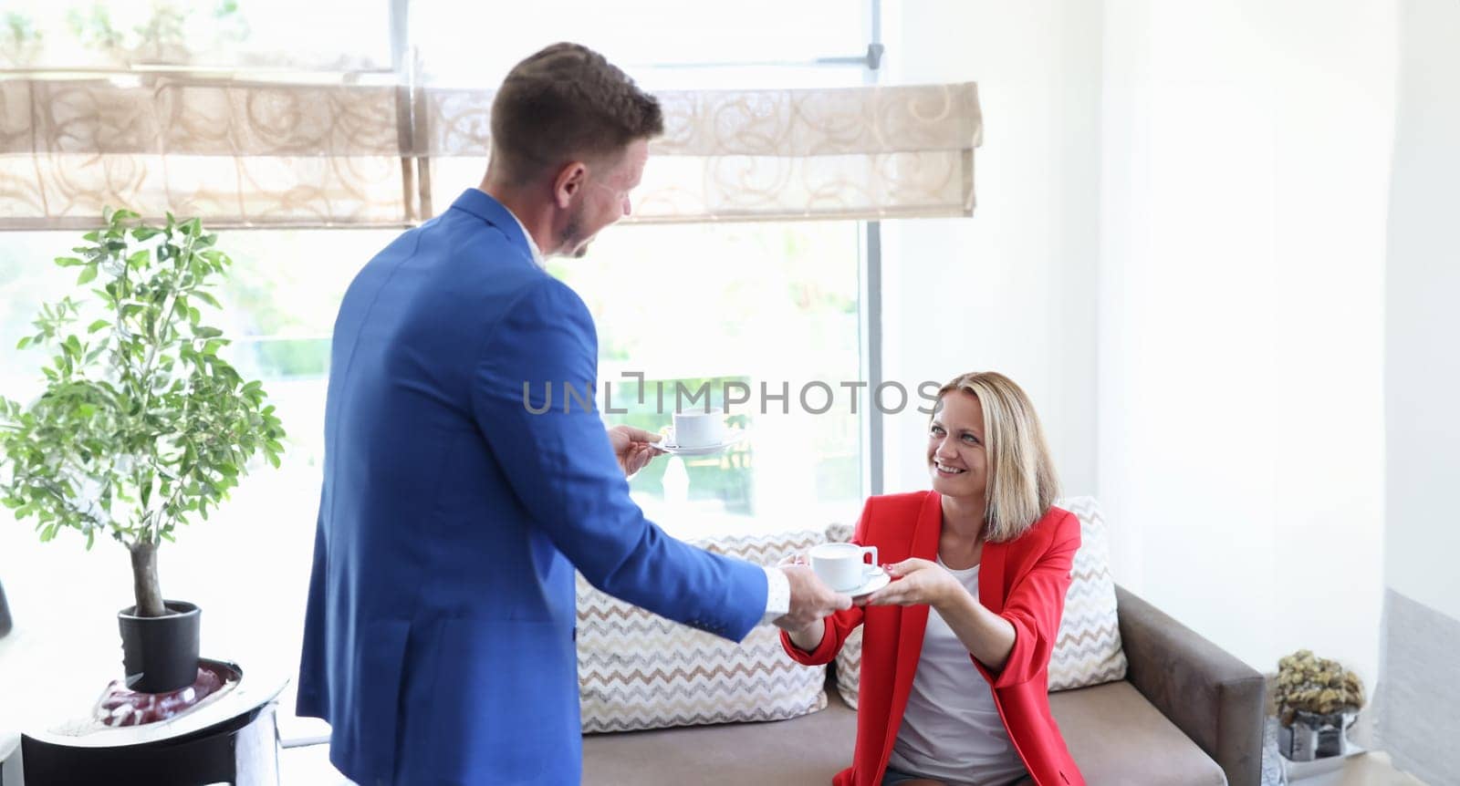 Man giving woman cup of coffee in office by kuprevich