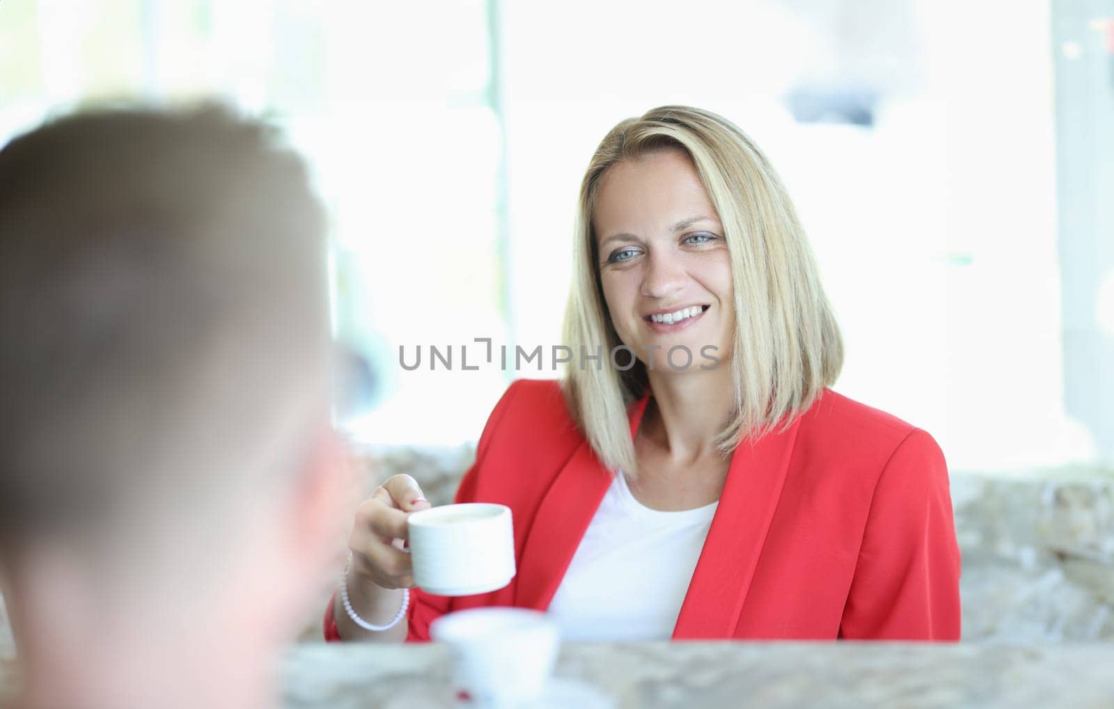 Woman in red jacket drinking coffee with man. Joint tea party concept