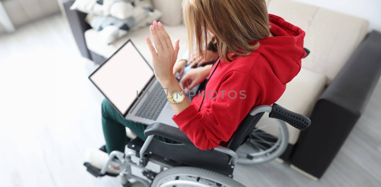 Disabled woman in wheelchair waving hand at laptop screen by kuprevich