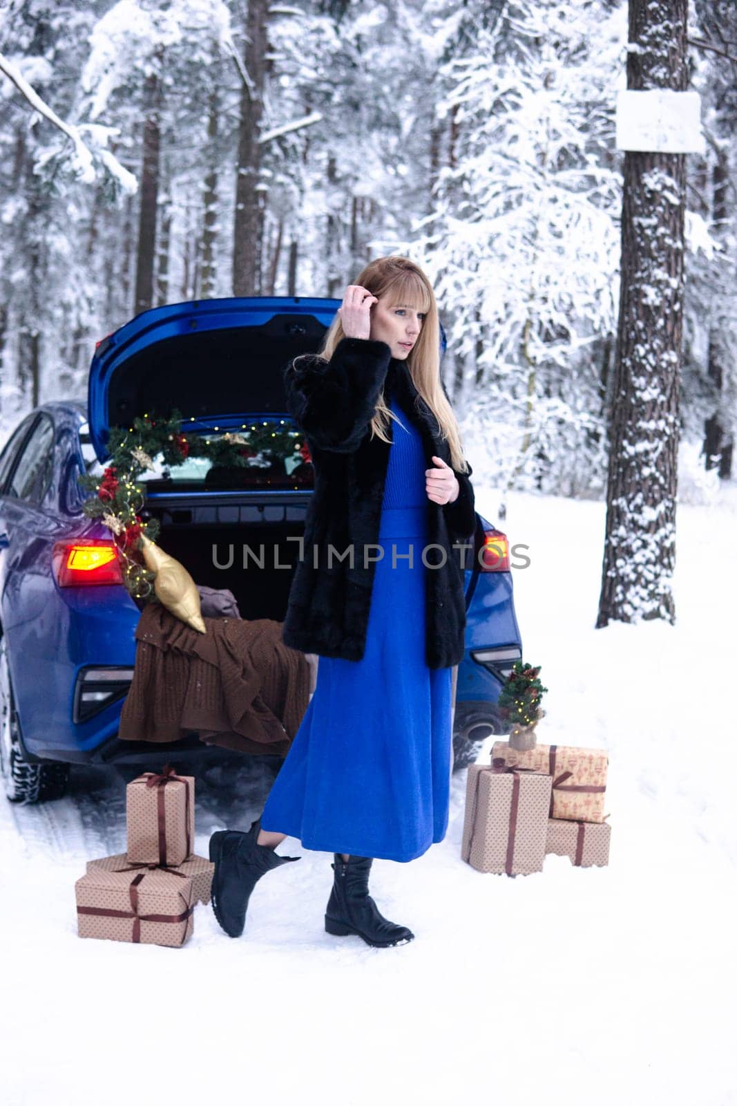 Woman in winter snowy forest in blue dress next to blue car decorated with Christmas decor. Christmas and winter holidays concept. by Annu1tochka