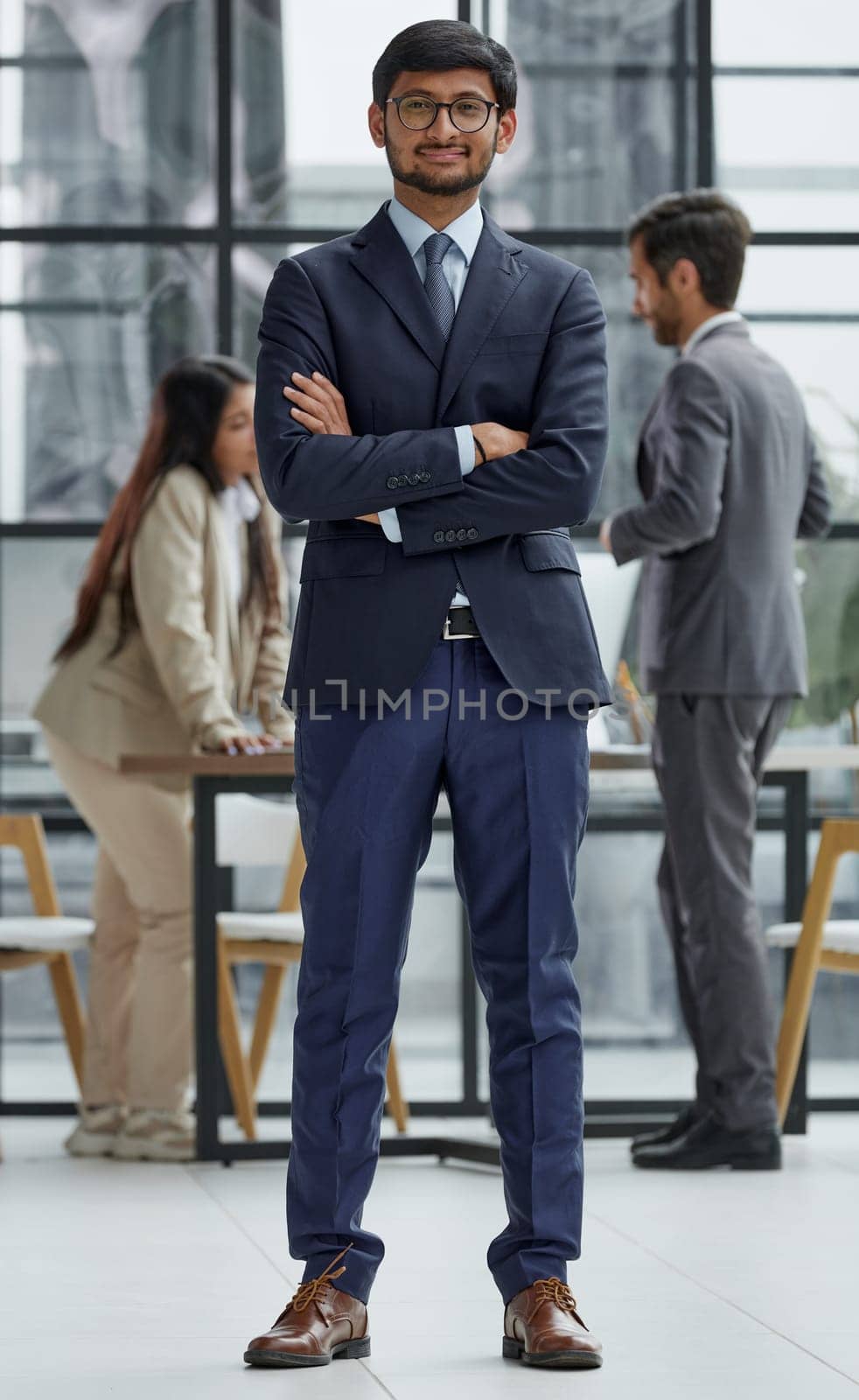 Handsome young business man in glasses standing confidently in the office by Prosto