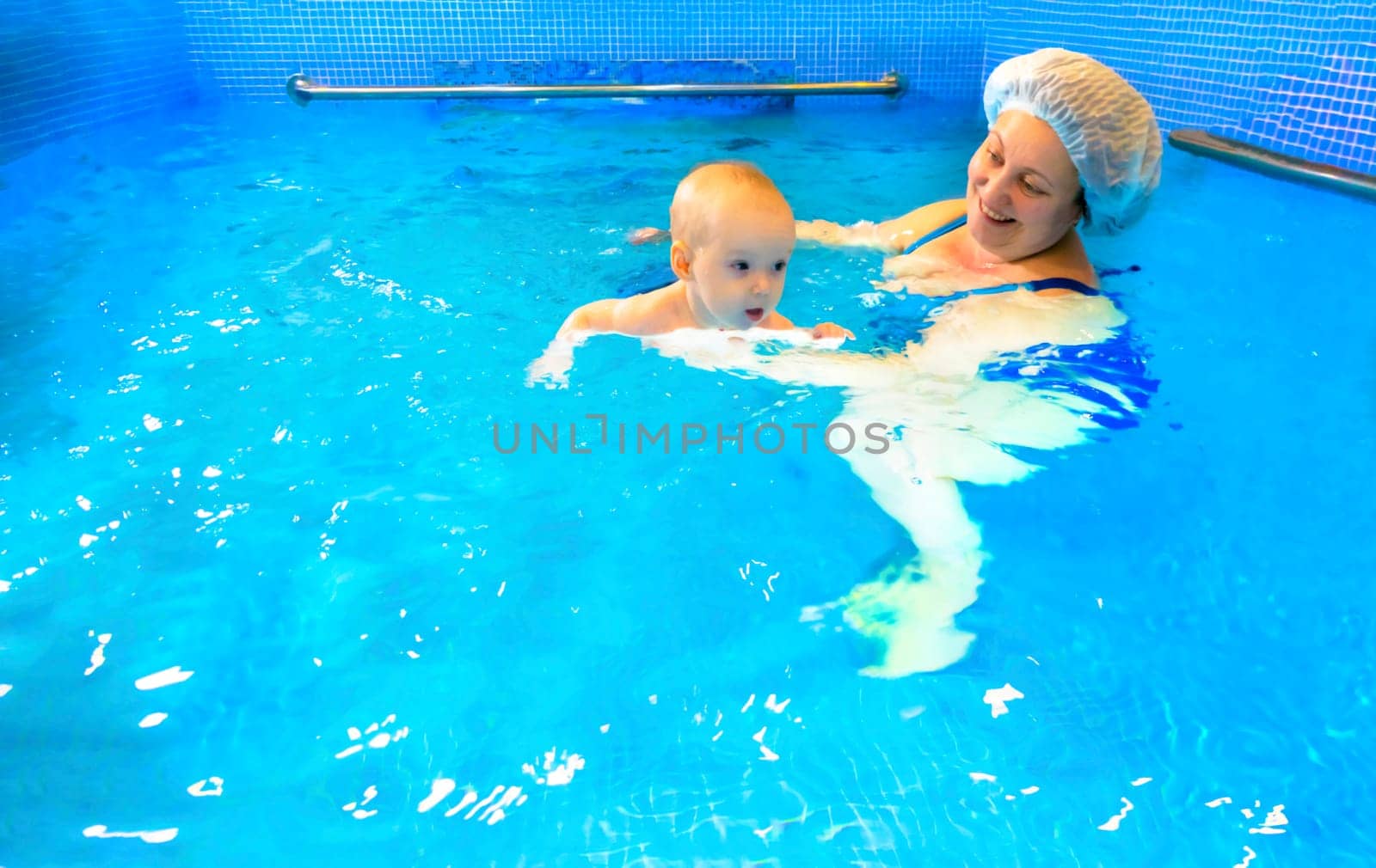 Adorable baby girl enjoying swimming in a pool with her mother early development class for infants teaching children to swim and dive. by kajasja