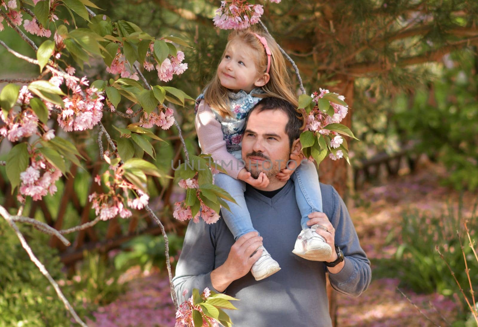 Father and daughter in a flowering garden with pink sakura by Godi
