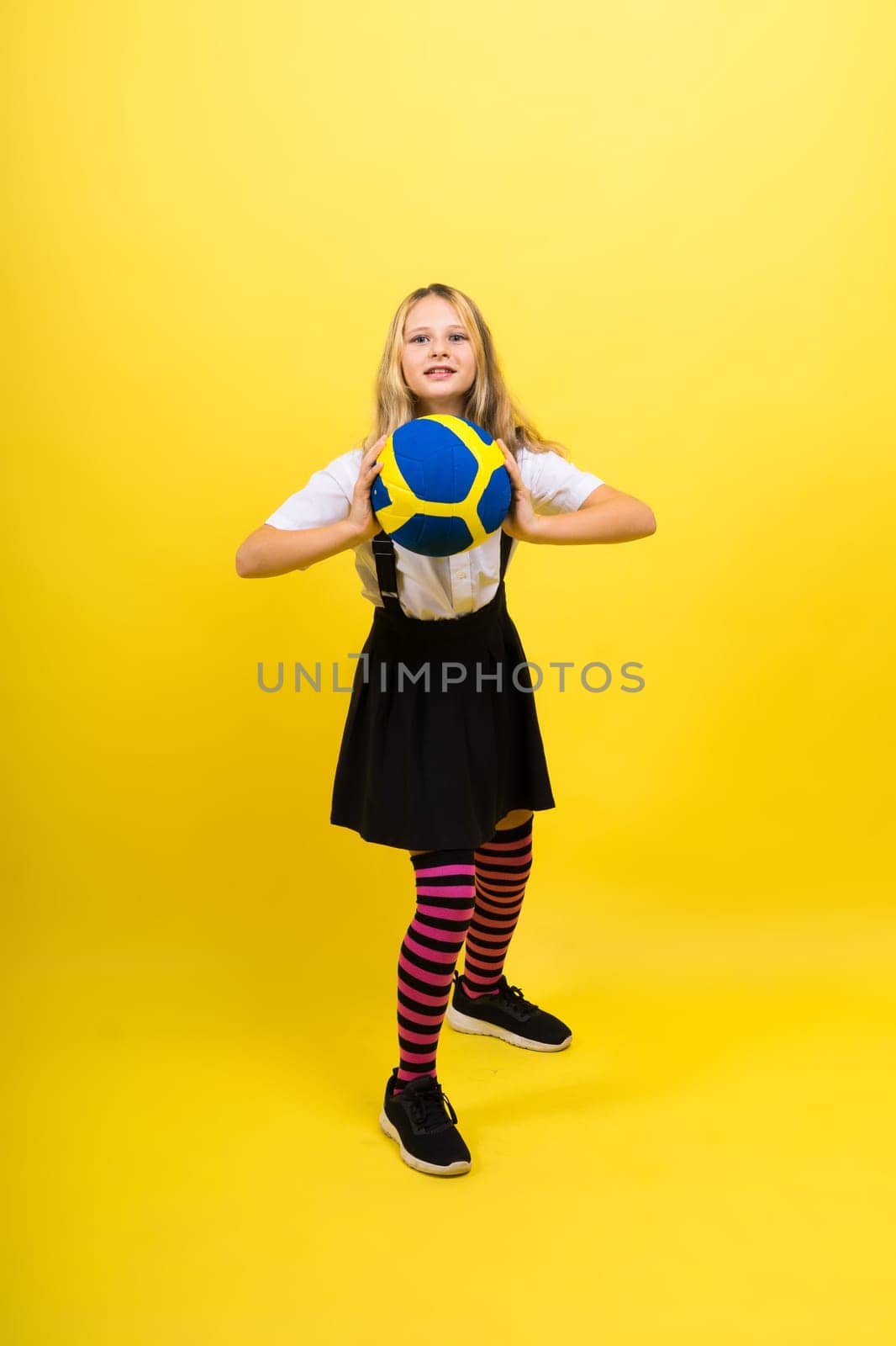 A teenager girl holds volleyball ball in hand and smiles on red yellow background. Studio photo.