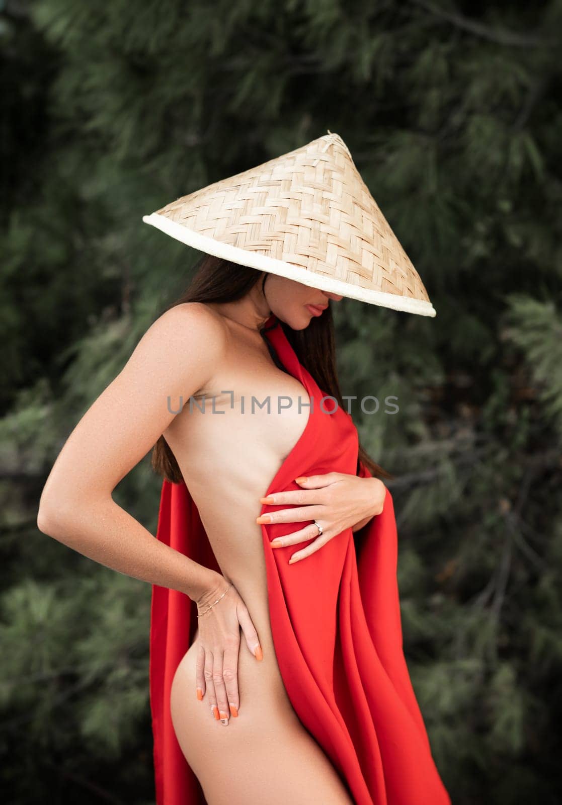 naked sexy woman in red fabric and Asian triangular hat on the background of nature