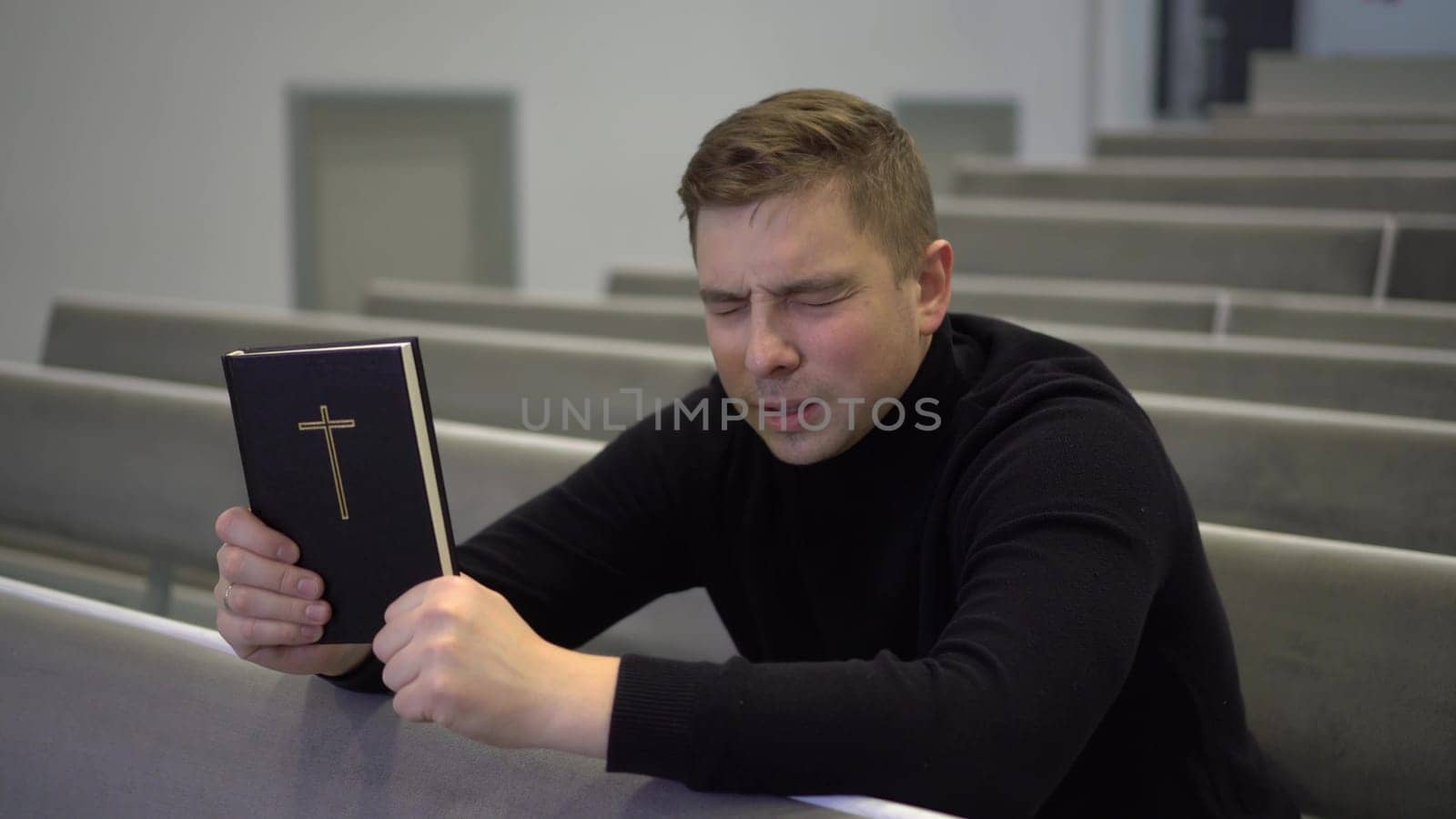 A young man prays holding a bible in his hands in a church. A Protestant man sits on a church bench and sincerely prays. 4k