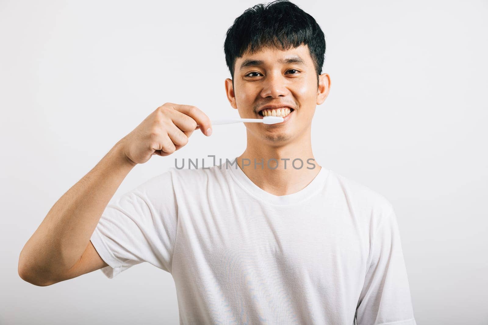 Asian young man demonstrates proper toothbrushing for dental health with a confident smile by Sorapop