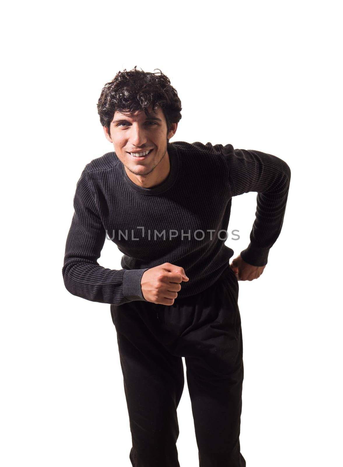 A handsome young man in a black sweater and black pants, running towards the camera, smiling, isolated on white